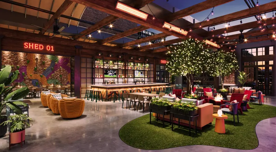 A Washington Avenue food hall at dusk, with a long bar, string lights and planted seating